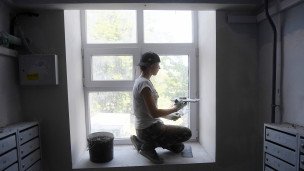 Маляр шпаклюет окно во время капитального ремонта в подъезде