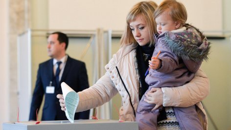 Женщина с ребенком на руках опускает бюллетень в урну для голосования