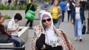 Женщина в солнцезащитных очках и платке говорит по телефону