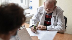 пациент на приеме у врача, врач пожилой мужчина в очках записывает 