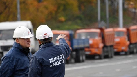 Двое мужчин в касках и форе с надписью Дороги и мосты указывают на дорогу