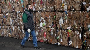 Сотрудник мусоросортировочного комплекса проходит вдоль блоков сырья