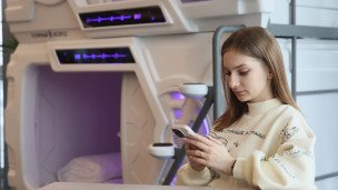 Девушка у капсулы для сна с телефоном в руках