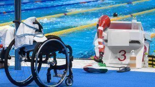 Протез и инвалидная коляска у стартовой тумбы во время тренировки спортсменов перед началом соревнований по плаванию