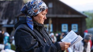 Пожилая женщина с книгой на фоне деревянного дома