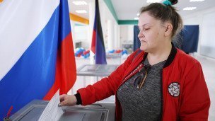 Женщина опускает бюллетень в урну прсле голосования