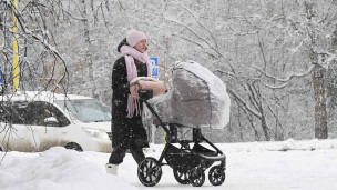 женщина с ребенком в коляске на прогулке в заснеженном парке