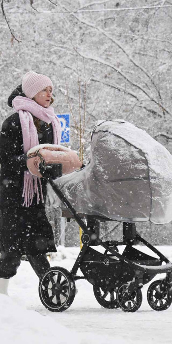 женщина с ребенком в коляске на прогулке в заснеженном парке