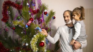 мужчина с ребенком на руках украшает елку